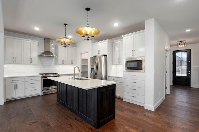 kitchen featuring wall chimney range hood, dark wood-type flooring, stainless steel appliances, and a sink