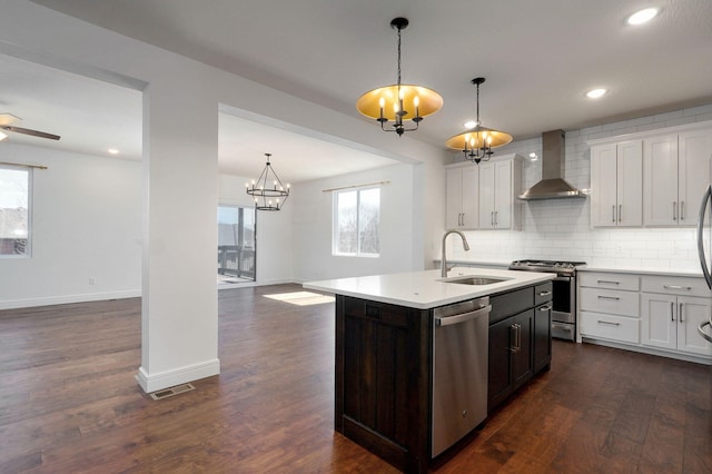 kitchen featuring dark wood-style flooring, a sink, light countertops, wall chimney range hood, and appliances with stainless steel finishes