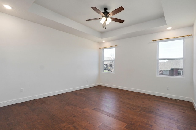 empty room with dark wood-style floors, baseboards, a tray ceiling, and ceiling fan