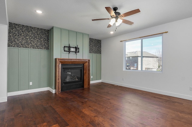 unfurnished living room featuring dark wood-style floors, a glass covered fireplace, a wainscoted wall, and recessed lighting