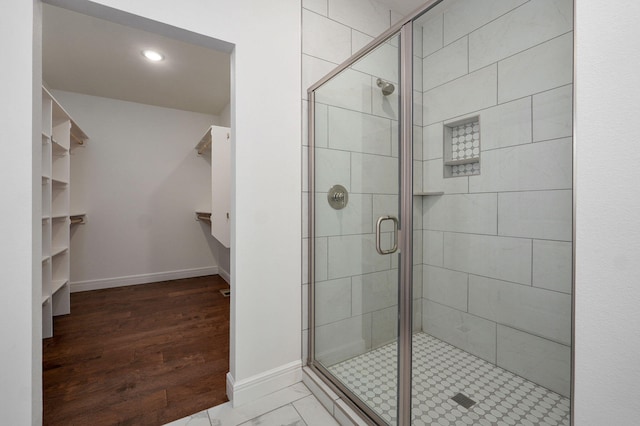 full bathroom with a spacious closet, a stall shower, wood finished floors, and baseboards