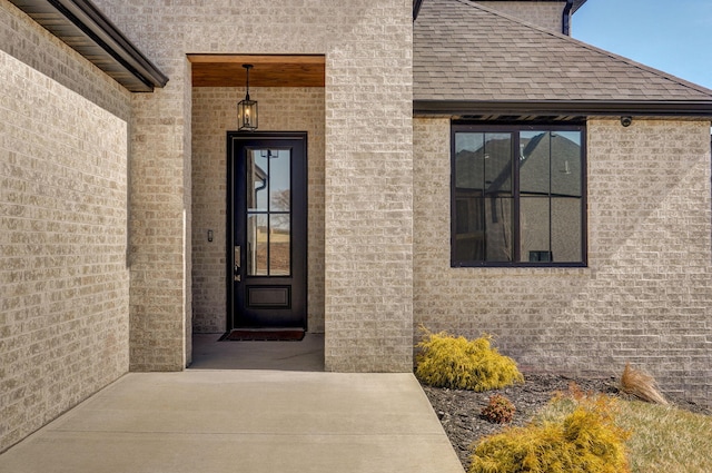 view of exterior entry with a shingled roof and brick siding