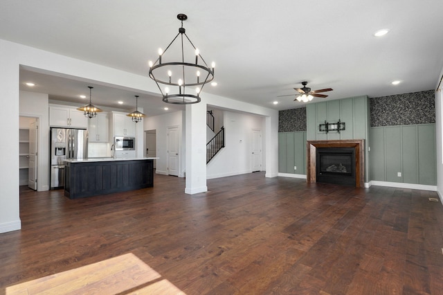 unfurnished living room with dark wood-style floors, recessed lighting, ceiling fan with notable chandelier, a glass covered fireplace, and stairs