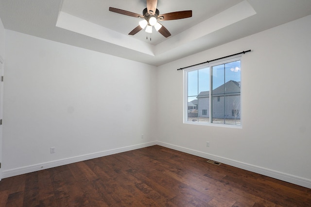 spare room with a tray ceiling, visible vents, ceiling fan, wood finished floors, and baseboards