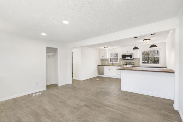 kitchen featuring stainless steel appliances, wood finished floors, white cabinetry, dark countertops, and crown molding