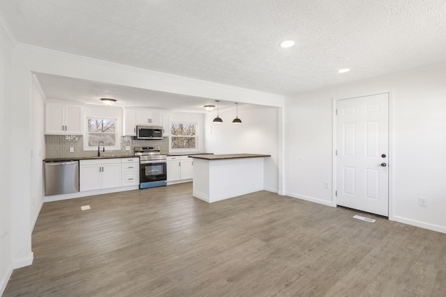 kitchen featuring a textured ceiling, wood finished floors, white cabinetry, appliances with stainless steel finishes, and dark countertops