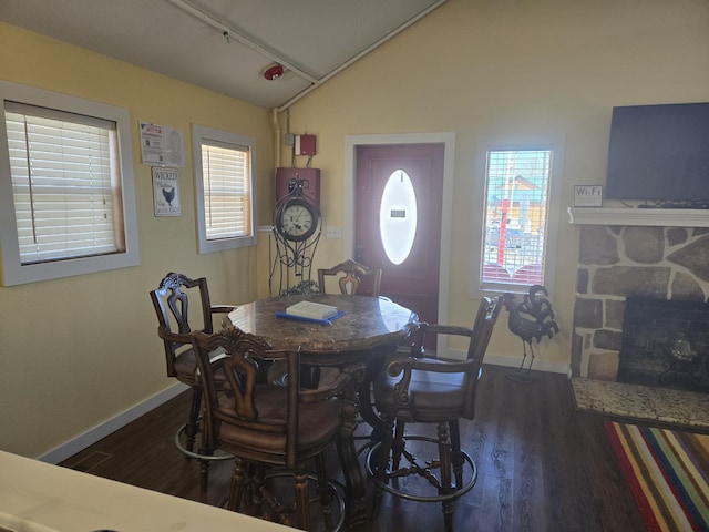 dining room with vaulted ceiling, a stone fireplace, baseboards, and wood finished floors