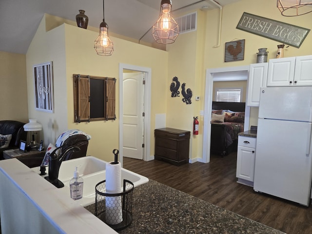 kitchen featuring visible vents, white cabinets, dark wood-type flooring, freestanding refrigerator, and vaulted ceiling