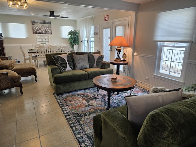 tiled living area featuring a ceiling fan and a wainscoted wall