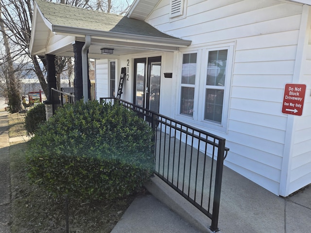 entrance to property with a shingled roof and a porch