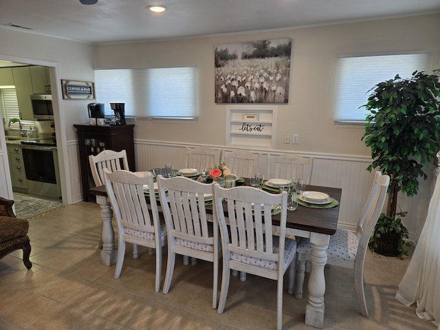 dining space featuring a wainscoted wall, tile patterned floors, and crown molding