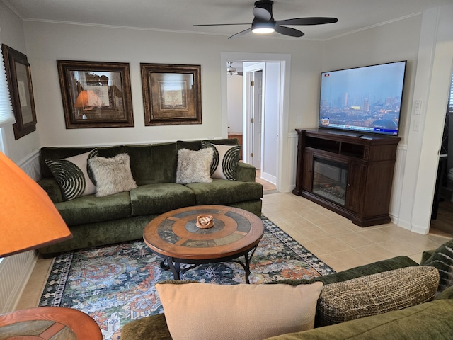 living room featuring ornamental molding, a glass covered fireplace, light tile patterned flooring, and ceiling fan