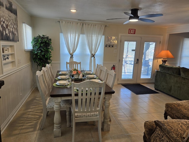 tiled dining area featuring french doors, wainscoting, built in shelves, and a ceiling fan