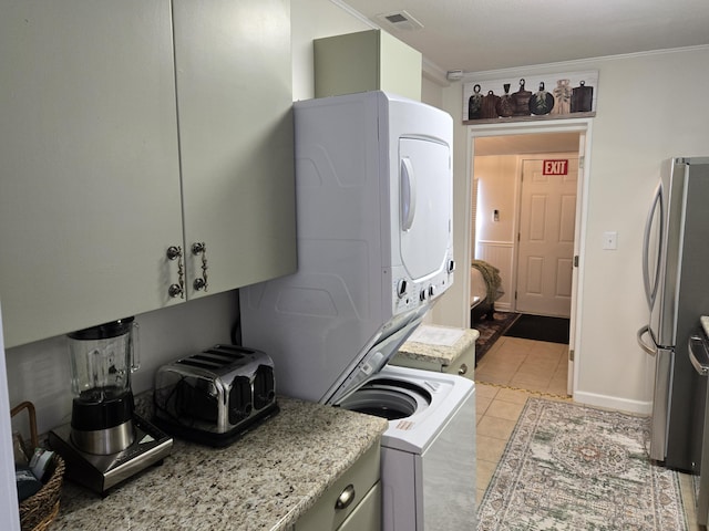 laundry area featuring light tile patterned floors, laundry area, visible vents, ornamental molding, and stacked washer and clothes dryer