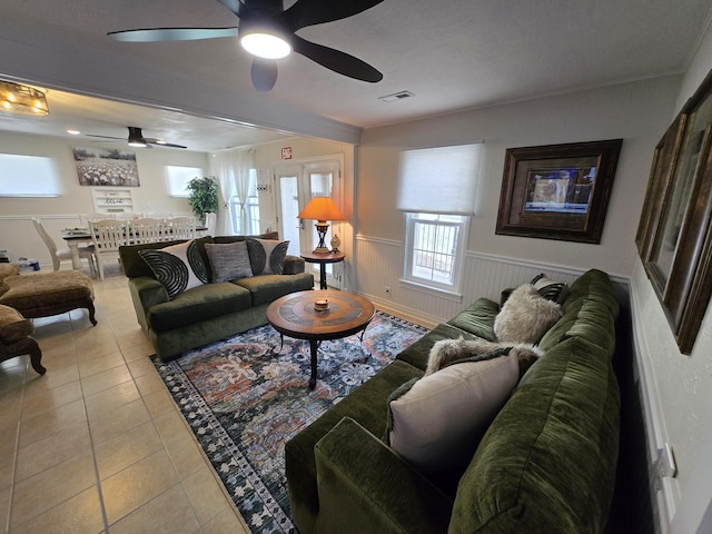 living room with tile patterned flooring, a wainscoted wall, ceiling fan, and visible vents