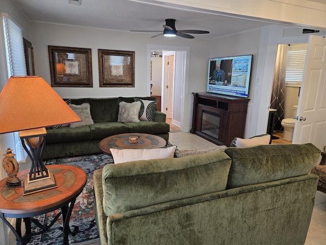 living area with ornamental molding, a glass covered fireplace, a ceiling fan, and light tile patterned floors