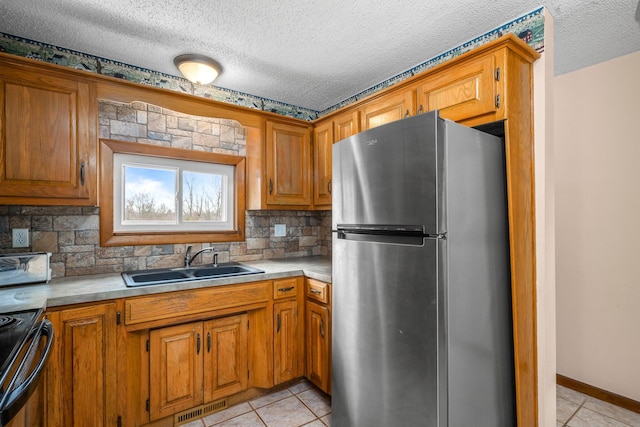 kitchen featuring light tile patterned floors, brown cabinets, a sink, and freestanding refrigerator