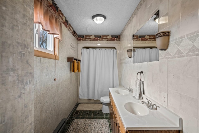 full bathroom featuring double vanity, a textured ceiling, tile walls, and a sink