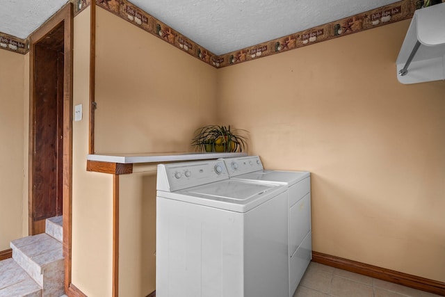 clothes washing area with a textured ceiling, light tile patterned floors, laundry area, baseboards, and washer and clothes dryer