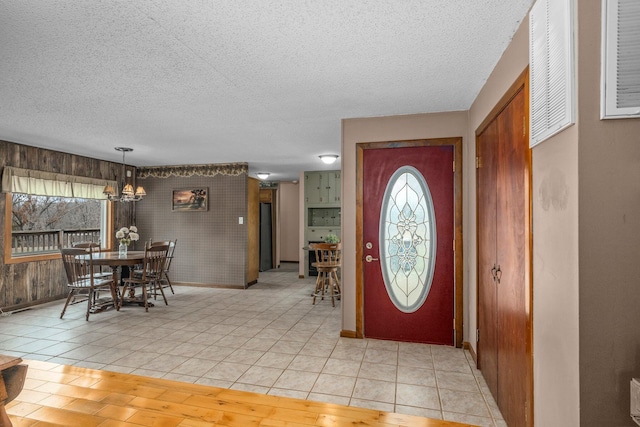 foyer entrance with light tile patterned floors, a notable chandelier, baseboards, and a textured ceiling