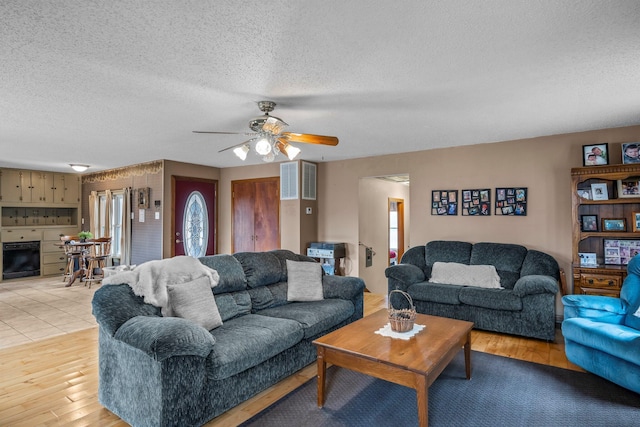 living area featuring light wood-style flooring, a fireplace, a ceiling fan, and a textured ceiling