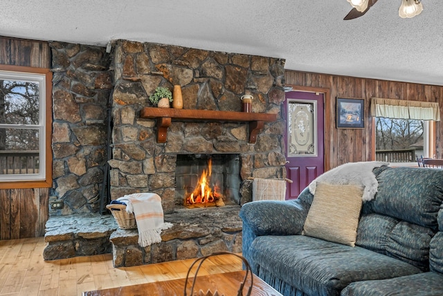 living room with a stone fireplace, plenty of natural light, hardwood / wood-style flooring, and wooden walls