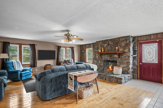 living area featuring a textured ceiling, a stone fireplace, wood finished floors, and a wealth of natural light