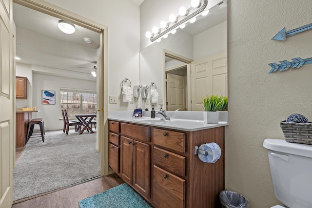 bathroom featuring a textured wall, toilet, ceiling fan, wood finished floors, and vanity