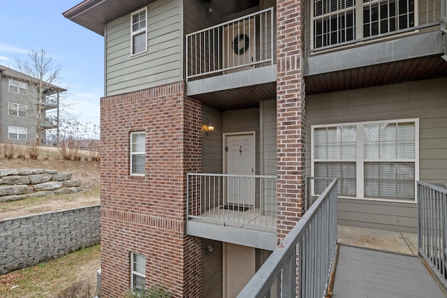 view of exterior entry with a balcony and brick siding