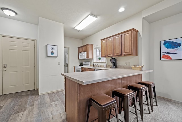 kitchen with white appliances, light wood-style flooring, a breakfast bar area, a peninsula, and light countertops