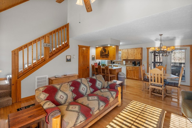 living area featuring stairs, visible vents, light wood-type flooring, baseboards, and ceiling fan with notable chandelier