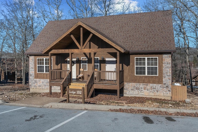 rustic home featuring uncovered parking, stone siding, a shingled roof, and board and batten siding