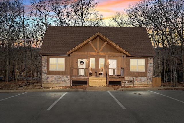 chalet / cabin with uncovered parking, stone siding, and a shingled roof