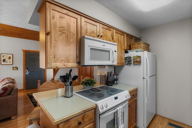 kitchen with brown cabinets, light countertops, a textured ceiling, light wood-type flooring, and white appliances