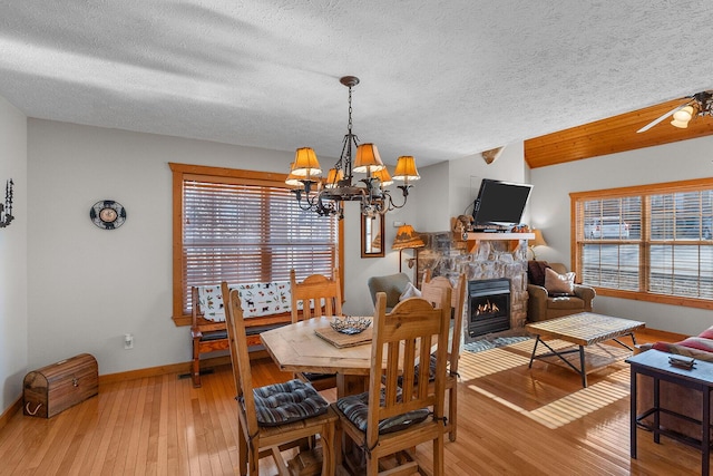 dining area featuring a textured ceiling, a fireplace, baseboards, light wood-style floors, and an inviting chandelier