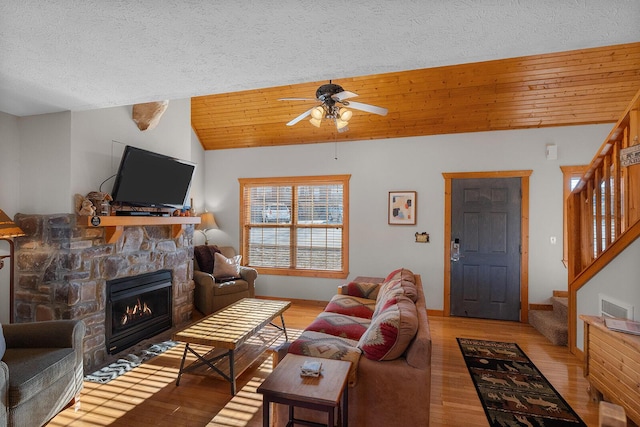 living room featuring a fireplace, light wood finished floors, stairway, wood ceiling, and vaulted ceiling