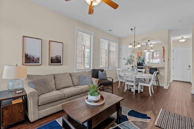 living room with ceiling fan with notable chandelier, arched walkways, baseboards, and wood finished floors