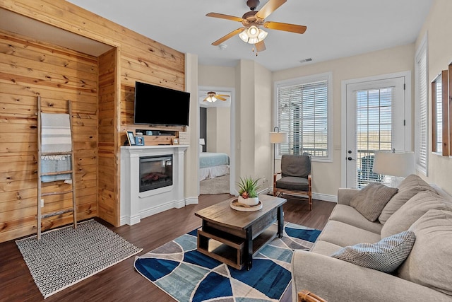 living room with dark wood-type flooring, visible vents, baseboards, a ceiling fan, and a glass covered fireplace