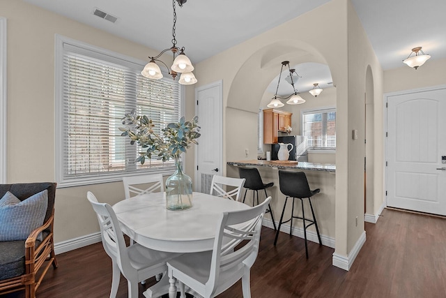 dining space featuring arched walkways, dark wood finished floors, visible vents, and baseboards