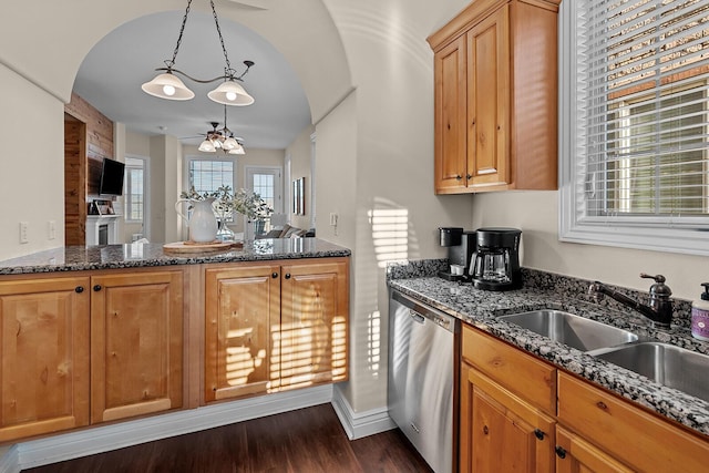 kitchen featuring dark wood-type flooring, dark stone counters, a sink, hanging light fixtures, and dishwasher