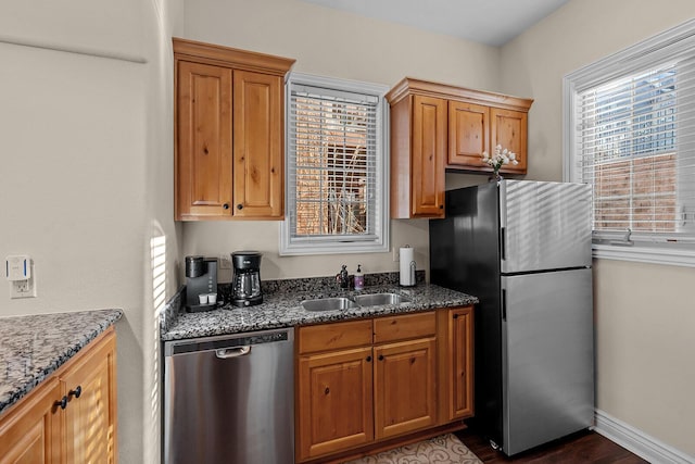 kitchen featuring brown cabinets, dark stone countertops, stainless steel appliances, and a sink