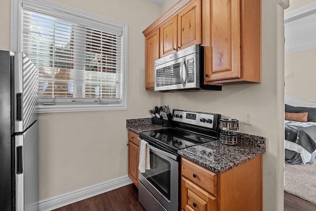 kitchen featuring stainless steel appliances, dark stone counters, dark wood finished floors, and baseboards