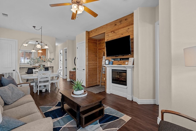 living area featuring arched walkways, dark wood-style flooring, a fireplace, visible vents, and ceiling fan with notable chandelier