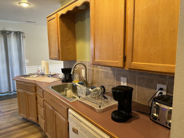 kitchen featuring decorative backsplash, white dishwasher, a sink, and wood finished floors