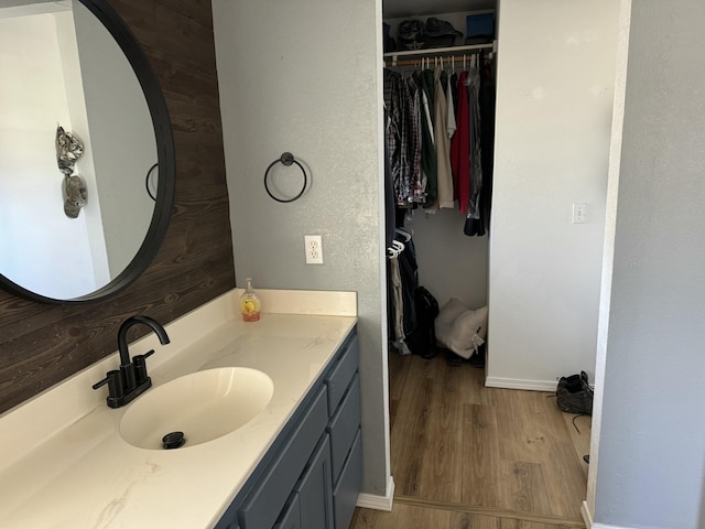 bathroom with baseboards, wood finished floors, vanity, and a walk in closet