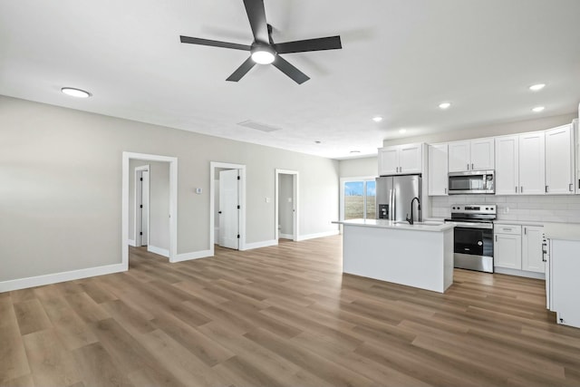 kitchen with a center island with sink, backsplash, light wood-style floors, appliances with stainless steel finishes, and light countertops