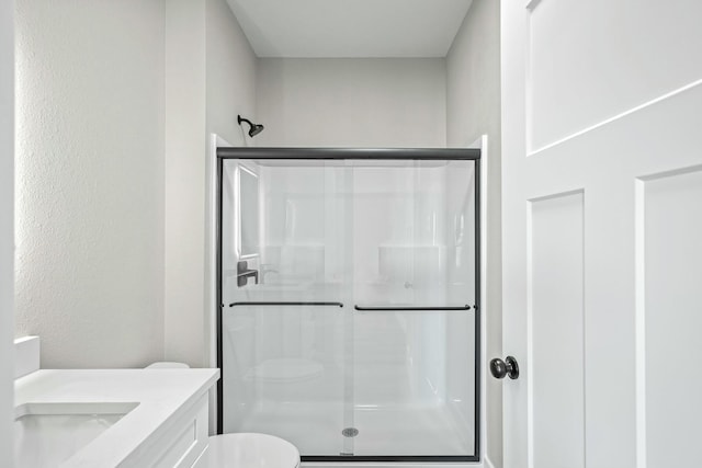 bathroom with a stall shower, toilet, vanity, and a textured wall