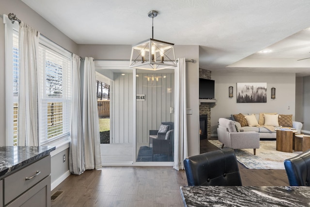 dining area with visible vents, baseboards, dark wood-style flooring, a stone fireplace, and a notable chandelier