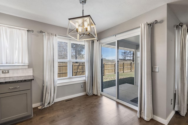 unfurnished dining area with dark wood finished floors, visible vents, plenty of natural light, and baseboards