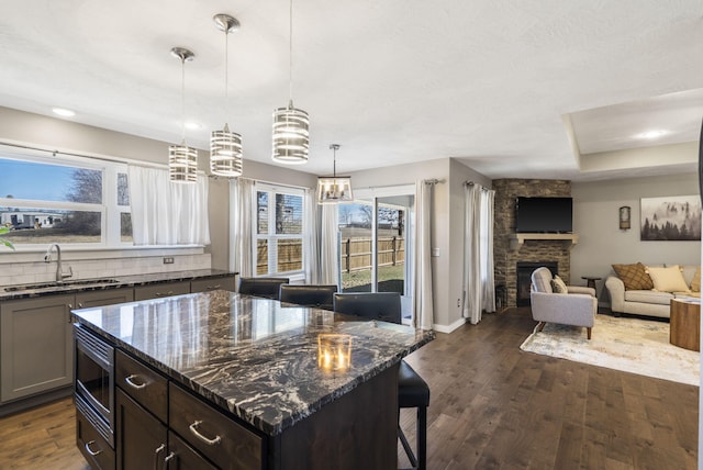 kitchen featuring a fireplace, a sink, dark wood-style floors, stainless steel microwave, and dark stone countertops